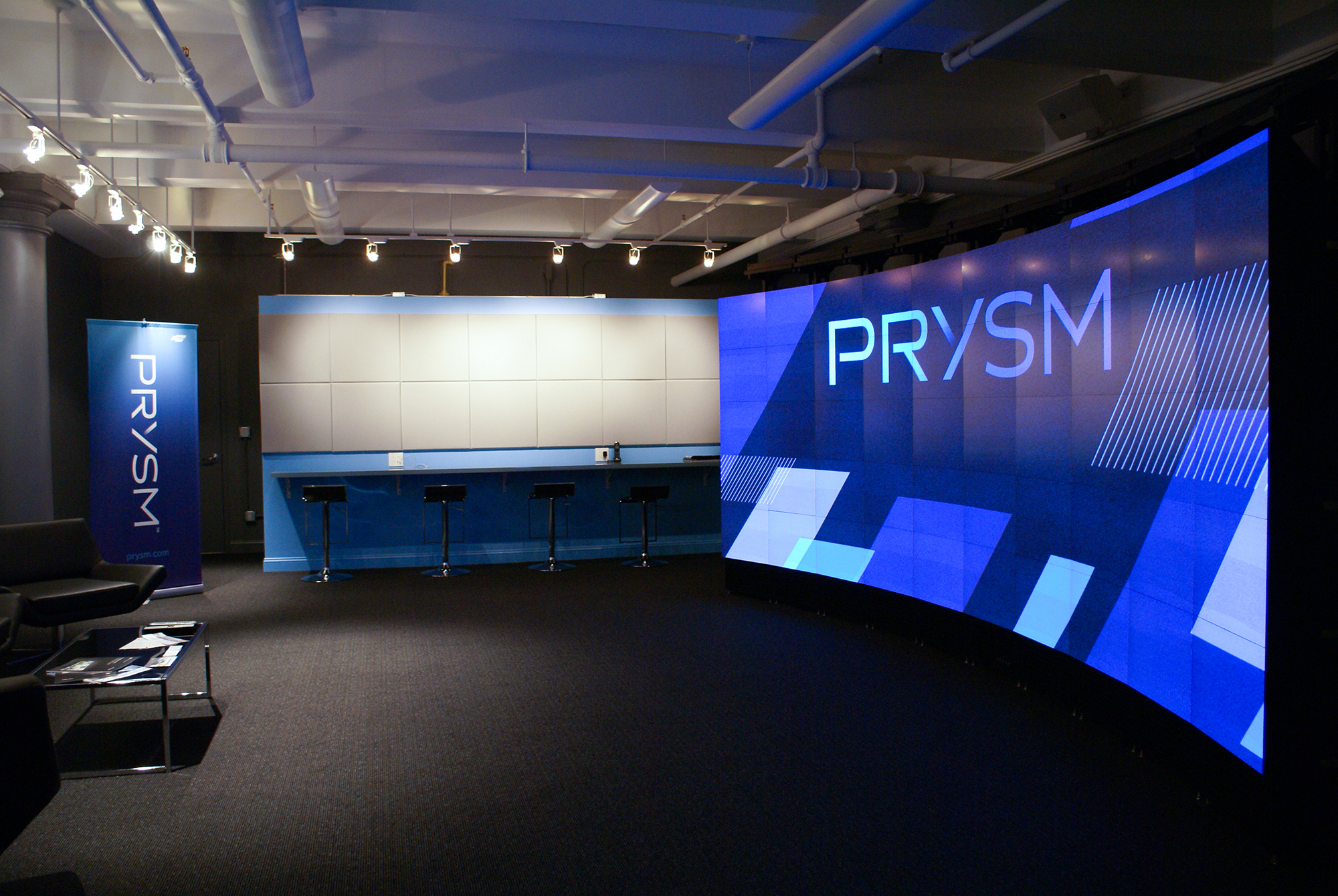 Showroom with wall sized siaply featuring prysm logo and spotlights against back wall